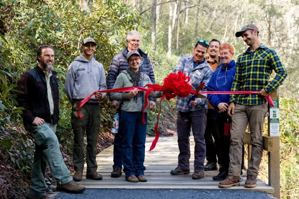 Staff and partners smile as Trail Crew Leader Michael Bagwell cuts the ribbon on the first trail bridge.